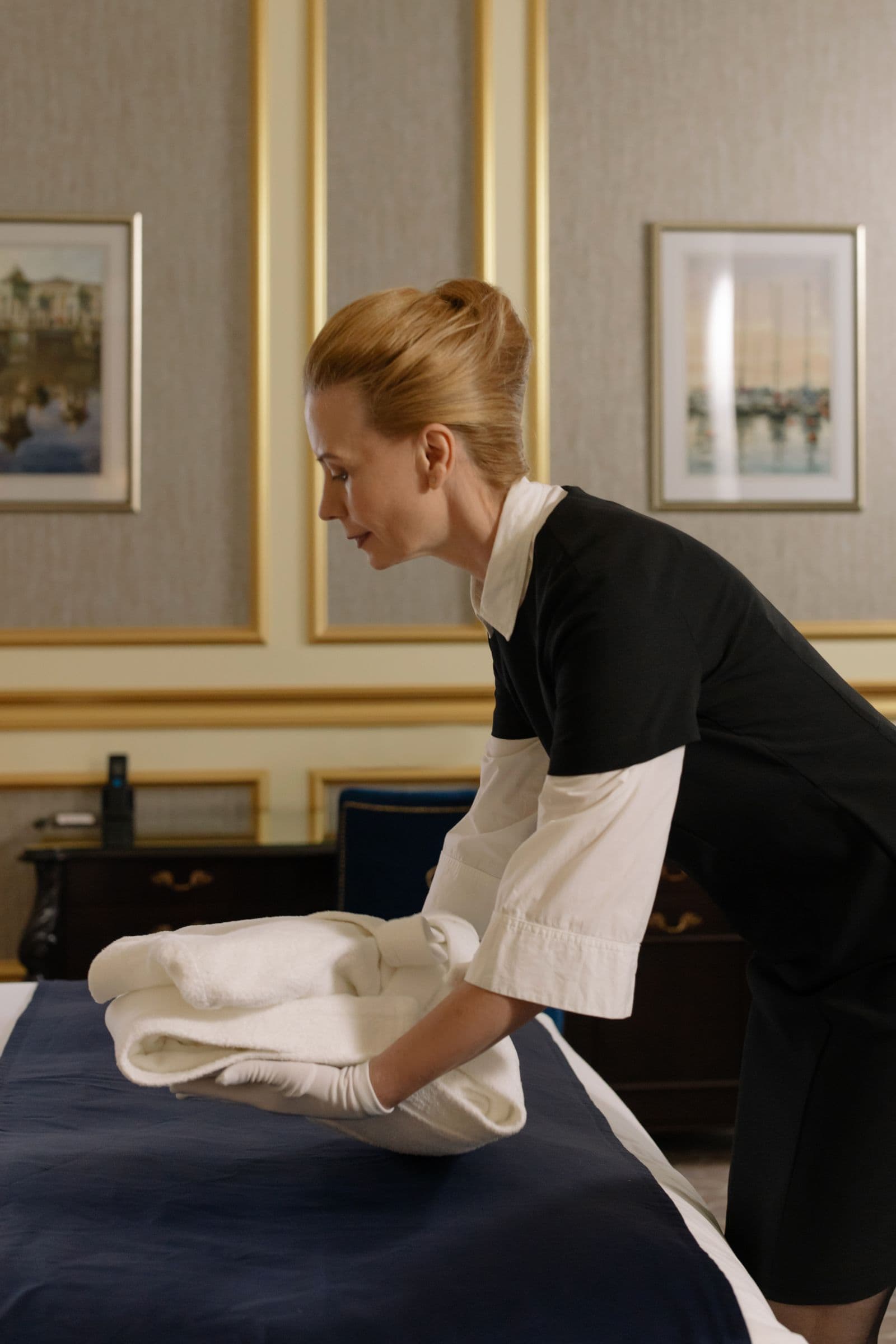 Femme de chambre en uniforme pliant du linge dans une chambre d'hôtel