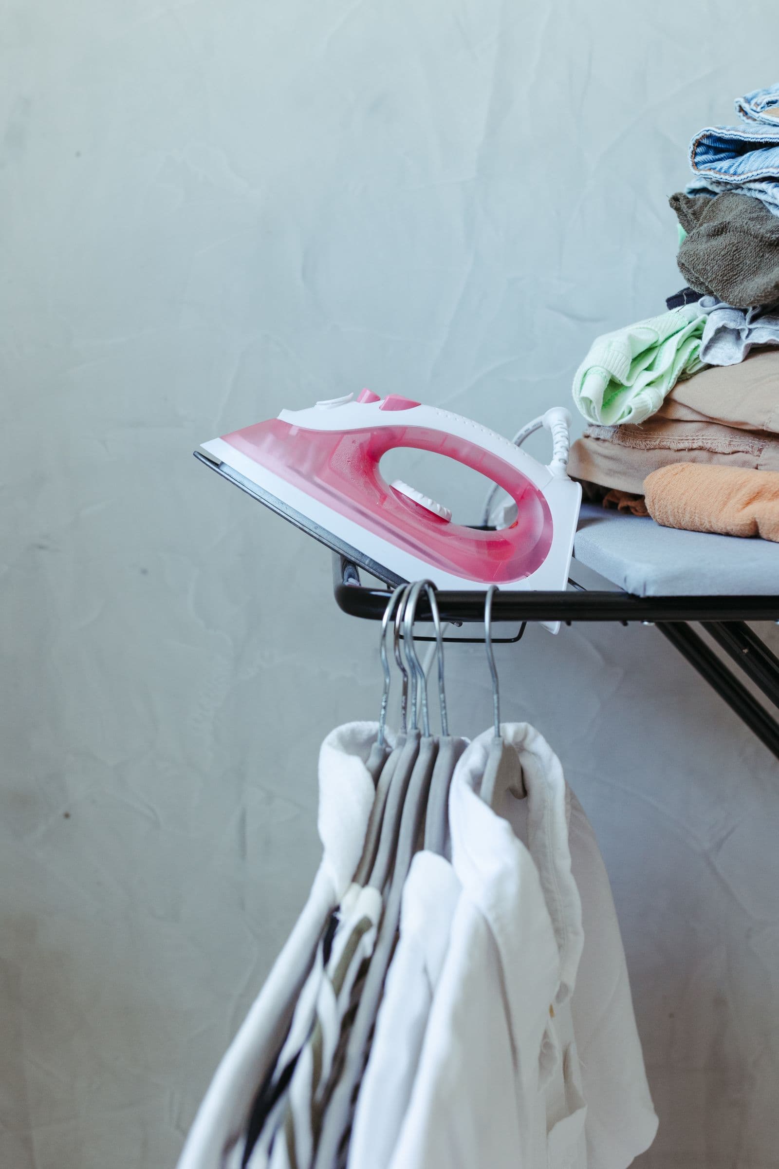 Fer à repasser sur la table, linge plié et cintres prêts